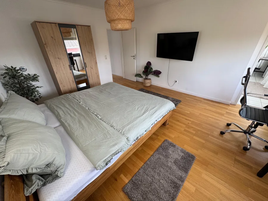 Helles Schlafzimmer einer Monteurunterkunft in NRW mit Doppelbett, TV und Arbeitsplatz