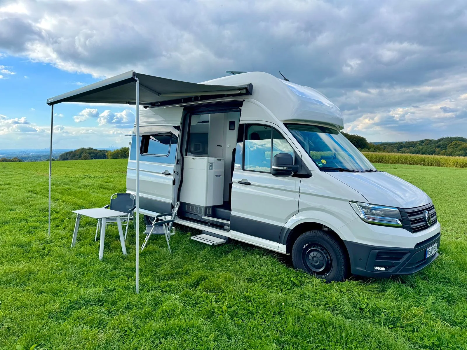 VW Grand California mit ausgefahrenem Vorzelt, geöffneter Seitentür und Campingmöbeln – perfektes Outdoor-Setup