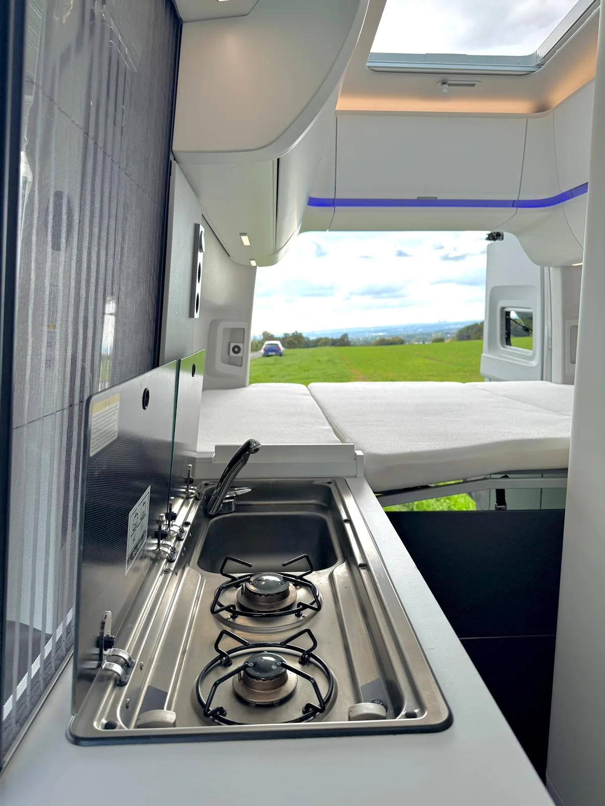 Zweiflammiger Edelstahl-Gaskocher mit integrierter Spüle und Blick auf das Doppelbett